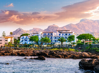 Fototapeta na wymiar summer beautiful view of nice hotel resort building in greek style on sea coast with amazing mountains and clouds on background of landscape