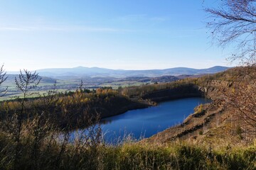 Blue quarry lake overlooks autumn landscape with distant mountains under a clear sky