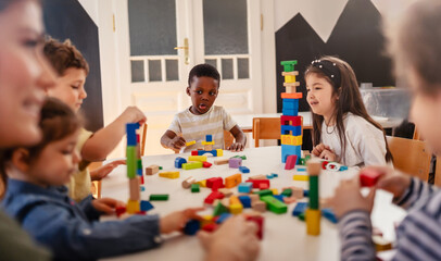 Group of diverse preschool children playing with colorful building blocks at a table in a bright,...