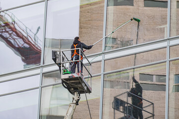 A worker in safety gear on a lift cleaning large glass windows of a modern building