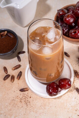 Healthy organic date seed coffee, iced coffee latte cup, made with grated date seeds, with whole date fruits and seeds on beige background . Alternative coffee hot drink