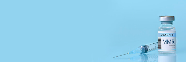 Bottle of MMR vaccine for measles, mumps, and rubella with a syringe placed on a blue background....