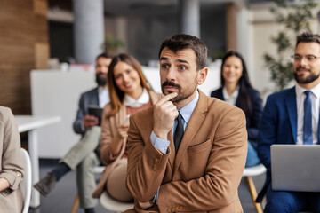 Portrait of focused businessman sitting at training room surrounded by his coworkers and listening...