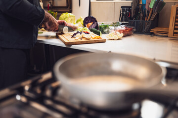 Close up of professional chef preparing ingredients for vegetarian meal in restaurant's kitchen. He is cutting onion.