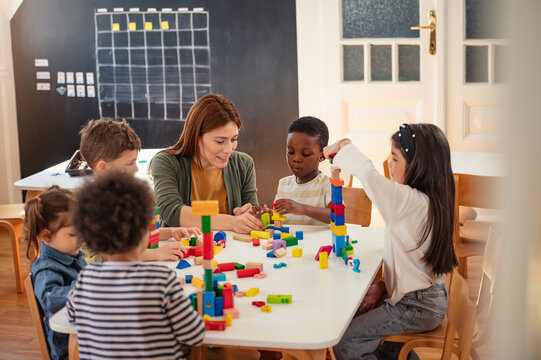 Diverse preschool children play with colorful building blocks at a classroom table, guided by a smiling teacher in a creative, inclusive early learning environment.