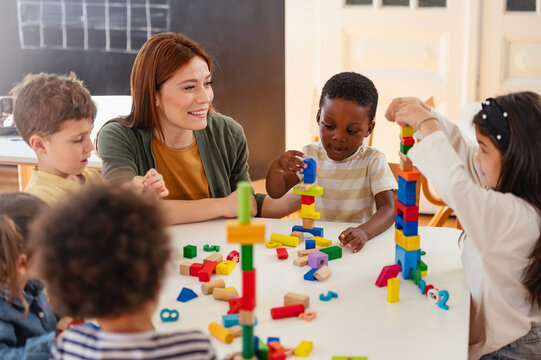 Diverse preschool children play with colorful building blocks at a classroom table, guided by a smiling teacher in a creative, inclusive early learning environment.