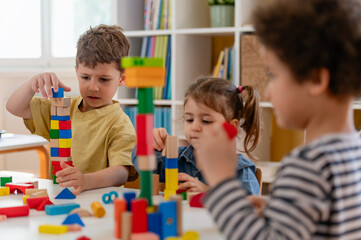 Group of diverse preschool children playing with colorful building blocks at a table in a bright, organized kindergarten classroom.