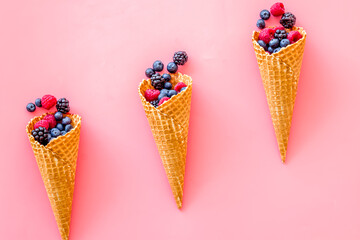 Fresh berries in waffle cones on pink background top view