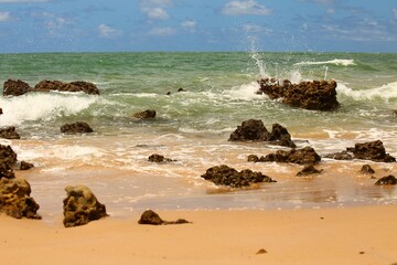 Green waters of a tropical beach in northeastern Brazil, with waves crashing against reef rocks, sunny day, summer vacation at Tabatinga beach, Joao Pessoa.