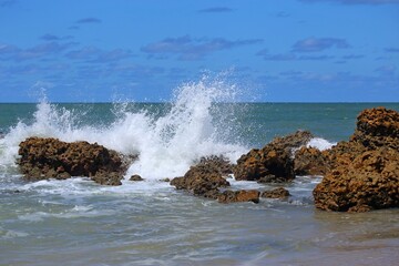
Sea waters crashing over reef rocks, sunny day, summer vacation at Tabatinga beach, Joao Pessoa, tropical beach in northeastern Brazil. Splashing with white foam over dark rocks