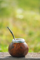 Mate tea in gourd calabash with bombilla close up on wooden table outdoor. Kettle with infused...