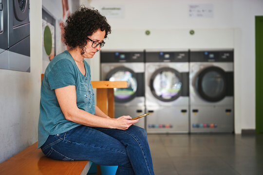 Woman using phone while waiting at self-service laundromat