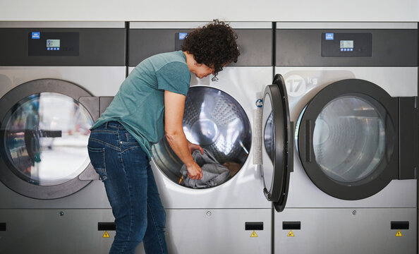 Woman loading clothes into industrial dryer at laundromat - Powered by Adobe
