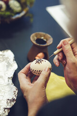 Woman hands painting Easter eggs with black bee wax, traditional Lithuanian method