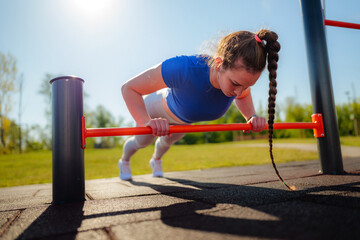 Fototapeta premium Concentrated sportswoman doing push ups on parallel bars in a calisthenics park, strengthening her upper body and core muscles in a sunny outdoor workout
