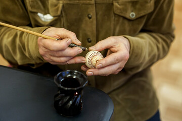 Woman hands painting Easter eggs with black bee wax, traditional Lithuanian method