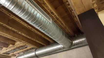 Exposed metal air duct system on a wooden ceiling with visible beams, showcasing industrial interior design elements and functional architectural details.