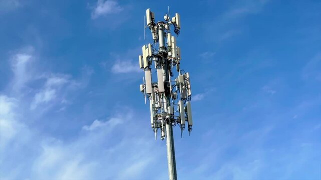 Cell phone microwave radio signal tower with a blue sky and wispy clouds in the background - time lapse