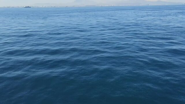 calm sea view from ferry boat with distant harbor and passing ships
