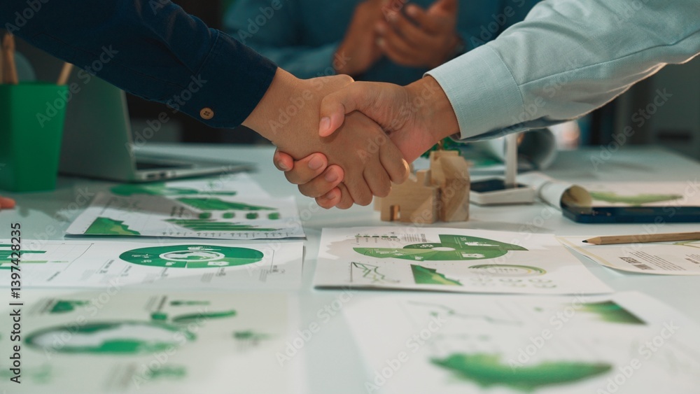 Poster a close-up of hands shaking over business strategy documents featuring graphs and charts, symbolizin