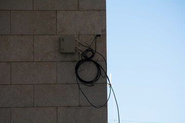 Utility cables hang on a building wall under clear blue sky during daytime in an urban setting