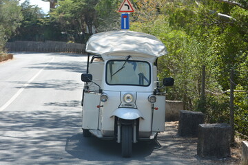 Classic white tuk-tuk parked on a quiet road surrounded by greenery on a sunny day