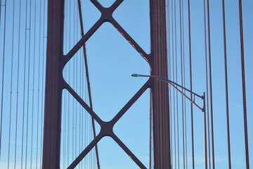 View of bridge cables against a clear blue sky with a streetlight in the foreground at midday