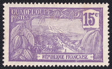 Issued in 1917, this French Guadeloupe stamp 15 centime shows cocoa pods, bananas and a view of the...