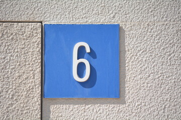 Number six displayed on a blue background on a textured wall during bright daylight