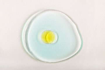 Fototapeta premium Close-up of yellow oil droplet on transparent serum drop on light background. Cosmetic or pharmaceutical product presentations. Concept of skincare or cosmetic product. Oil capsule on glass texture