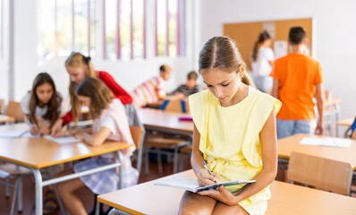 Portrait of schoolgirl with notebook in her hands who sits on desk in a school class