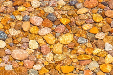 Flat textured surface filled with small rounded pebbles in mixed orange brown yellow tones forming natural mineral layer with visible rough pattern in macro closeup