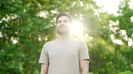 Happy young adult sportsman relaxing with closed eyes standing in urban city park. Smiling handsome fit man breathes deeply, feels relief and enjoys being in nature while resting after morning workout