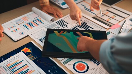 A diverse team collaborates in a modern office, engaging in data analysis. They use a digital tablet displaying colorful infographics while discussing charts and reports. SACTR