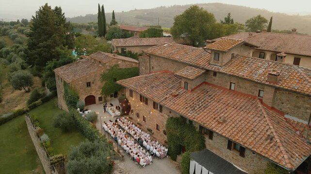 Drone shot of an outdoor wedding dinner in Tuscany, Italy near a villa with long tables, general plan with the villa Quercia al Poggio
