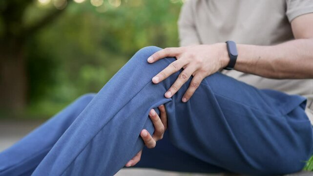 Close up. Sportsman hands holding massaging knee during a workout sitting on in an urban city park. The athlete suffers from painful severe knee joint pain, leg pain, calf muscle spasm, stretch pull