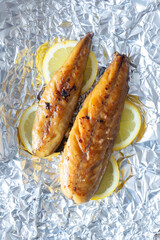 Smoked mackerel fillets cooked with sliced lemon on an aluminium background backdrop.