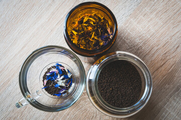 Dried cornflowers in glass, transparent cup used for tea. Edible flowers of Centaurea with intense blue, rose and white pigment. Organic tea idea. Granulated black tea mixed with cornflowers petals. 
