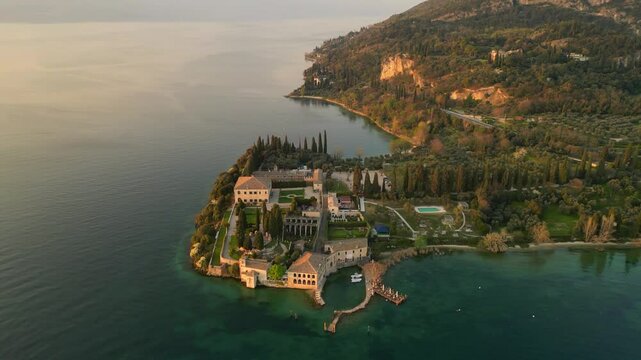 panoramic scenic aerial video of San Vigilio Point at Garda Lake Italy at sunset. Historical hotel villa, appetitive on the lake shore, destination travel 