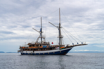 Naklejka premium Vintage-style sailing ship cruising on calm blue sea in Raja Ampat
