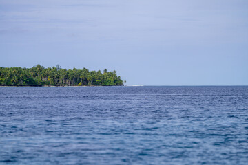 Distant view of a small tropical island covered in palm trees surrounded by endless ocean