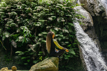 Tranquil moment as woman relaxes on mossy rock near cascading tropical waterfall