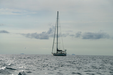 Lonely sailboat anchors in vast open sea beneath soft sky, evoking solitude and freedom of ocean...