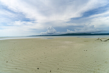 Empty tropical beach with rippled sand and dramatic clouds stretching to distant hills