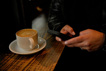 Woman using smartphone and drinking cappuccino in cafe