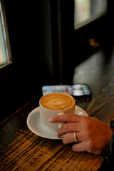 Woman holding cappuccino cup in cafe by window