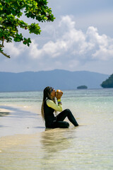 Woman in a wetsuit striking a confident pose on a tropical beach with turquoise water and lush green island