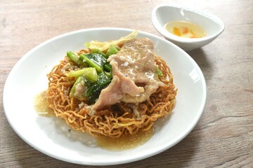 crispy fried egg noodle with slice soft marinated pork and Chinese kale dressing gravy sauce on plate couple vinegar chili cup