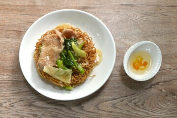 crispy fried egg noodle with slice soft marinated pork and Chinese kale dressing gravy sauce on plate couple vinegar chili cup