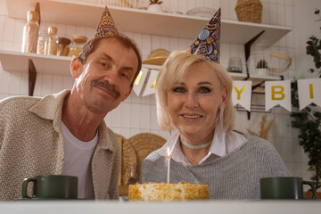 Senior couple wearing party hats celebrating birthday with cake at home